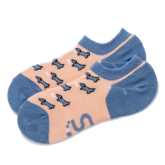 A pair of low-cut socks with a peach-colored body, blue/grey toes and heels, and a pattern dachshund dogs